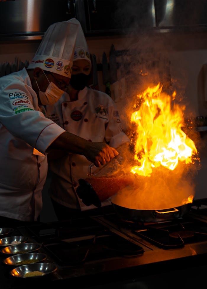 Chefs add flair with a blazing flambé technique in a modern kitchen setting. Perfect for culinary enthusiasts.